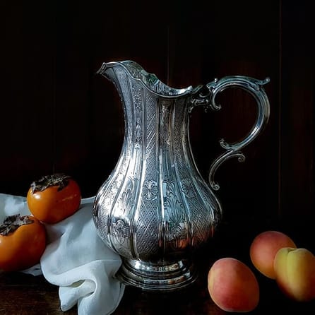 Still life of a silver water jug with fruit